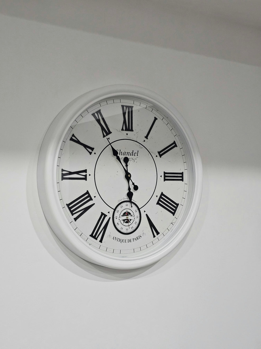 a white clock with roman numerals hanging from the ceiling