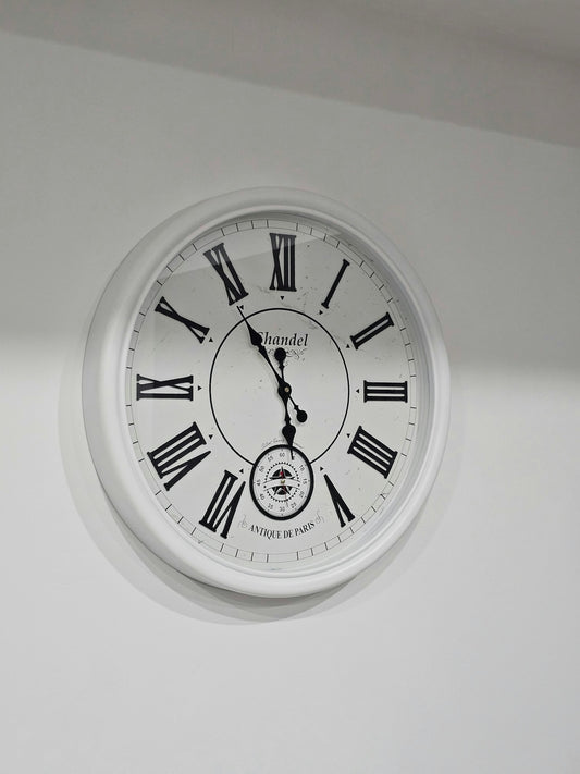 a white clock with roman numerals hanging from the ceiling
