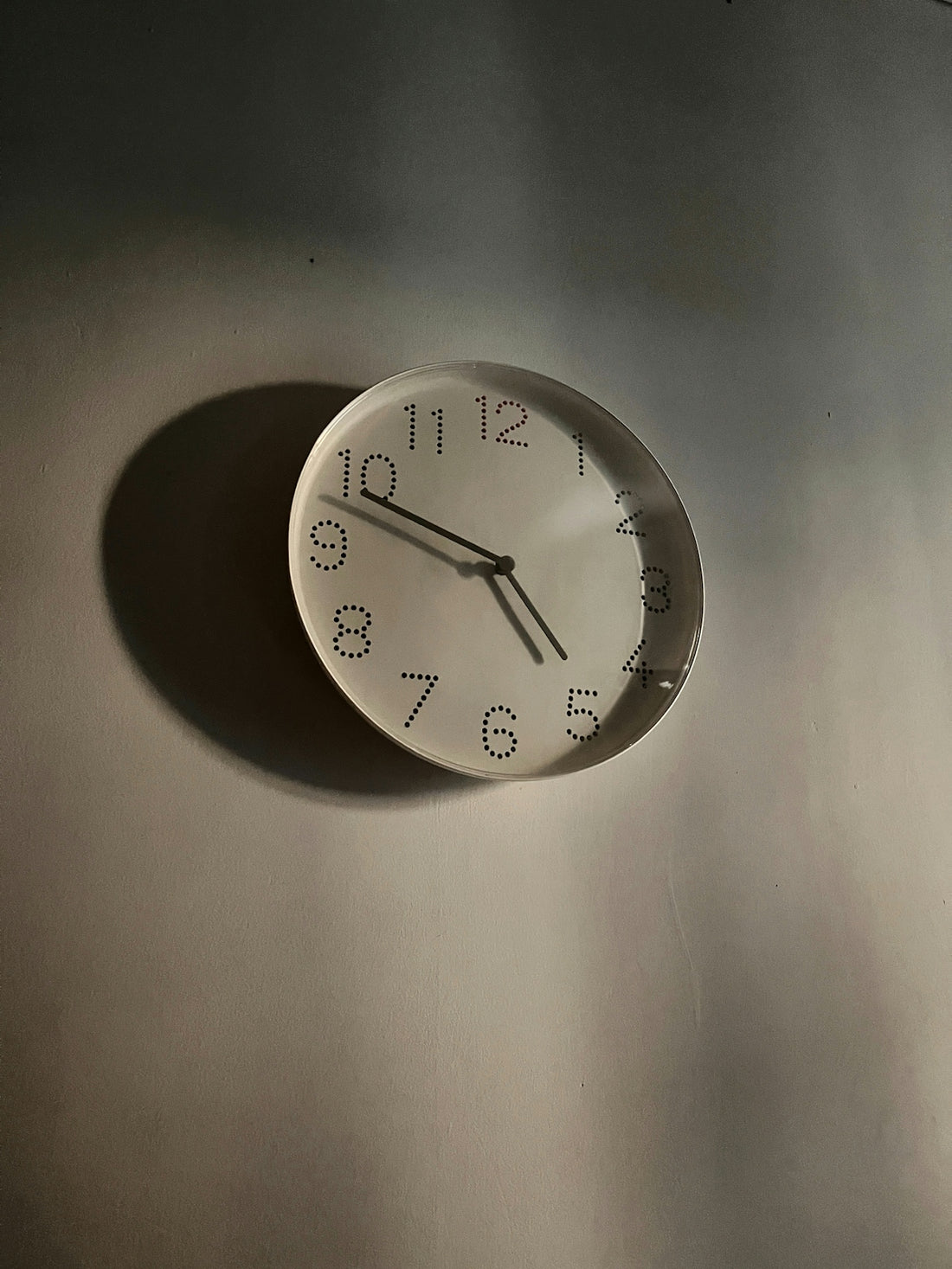 A simple clock casts a shadow on a wall.