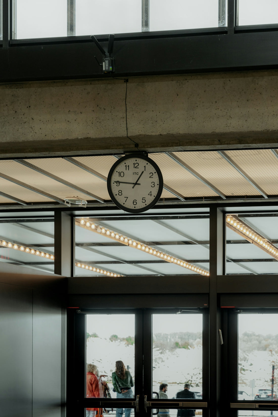 A clock hangs over a window, and people below.