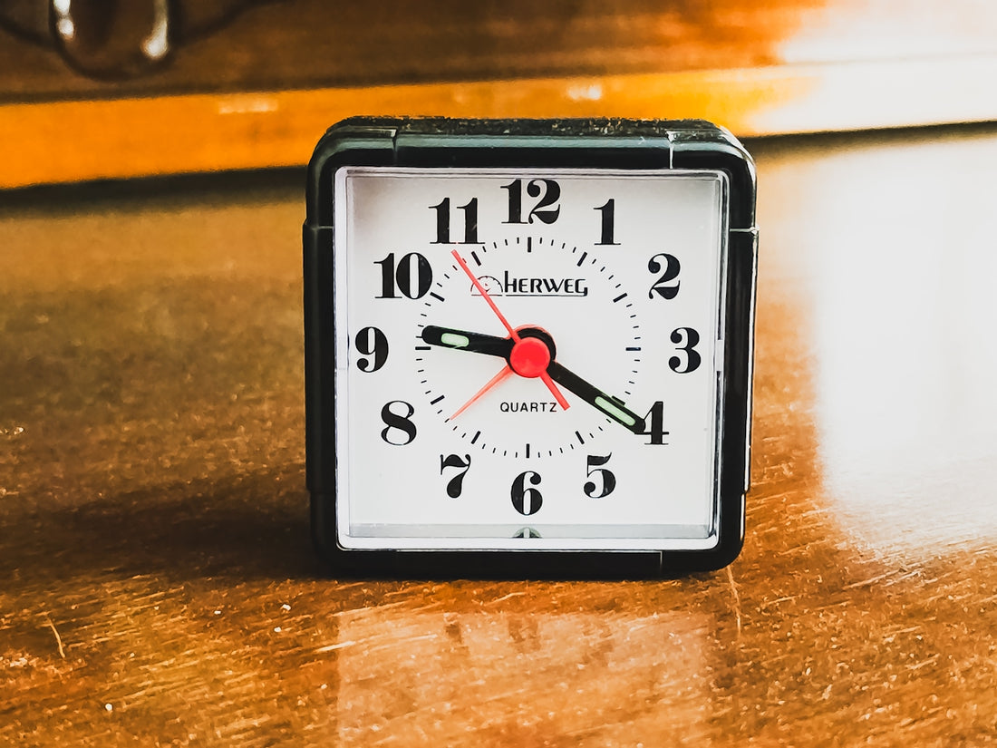 A small square alarm clock on a wooden surface.