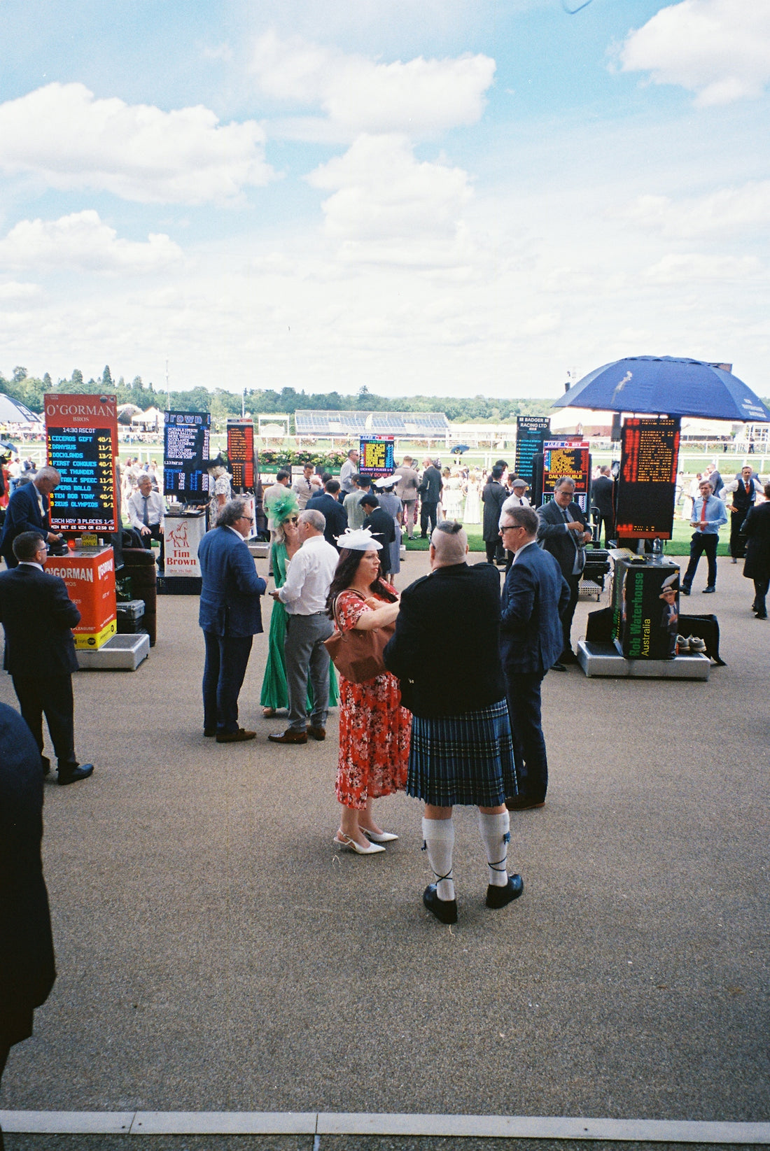 Racegoers with betting boards under a cloudy sky