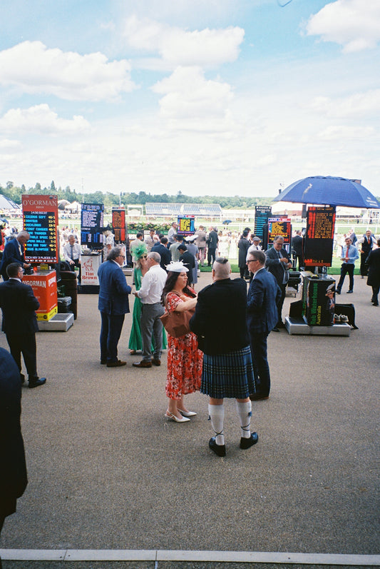 Racegoers with betting boards under a cloudy sky