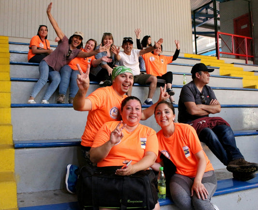 A group of people in orange shirts waving and smiling on stadium bleachers